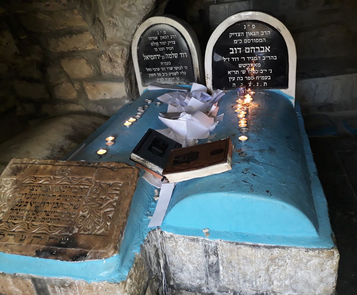 Inside the burial cave in Tzfas: the blue kever of the Bas Ayin with his headstone, the Arvei Nachal's headstone beside it, candles and kvitlach on the kever
